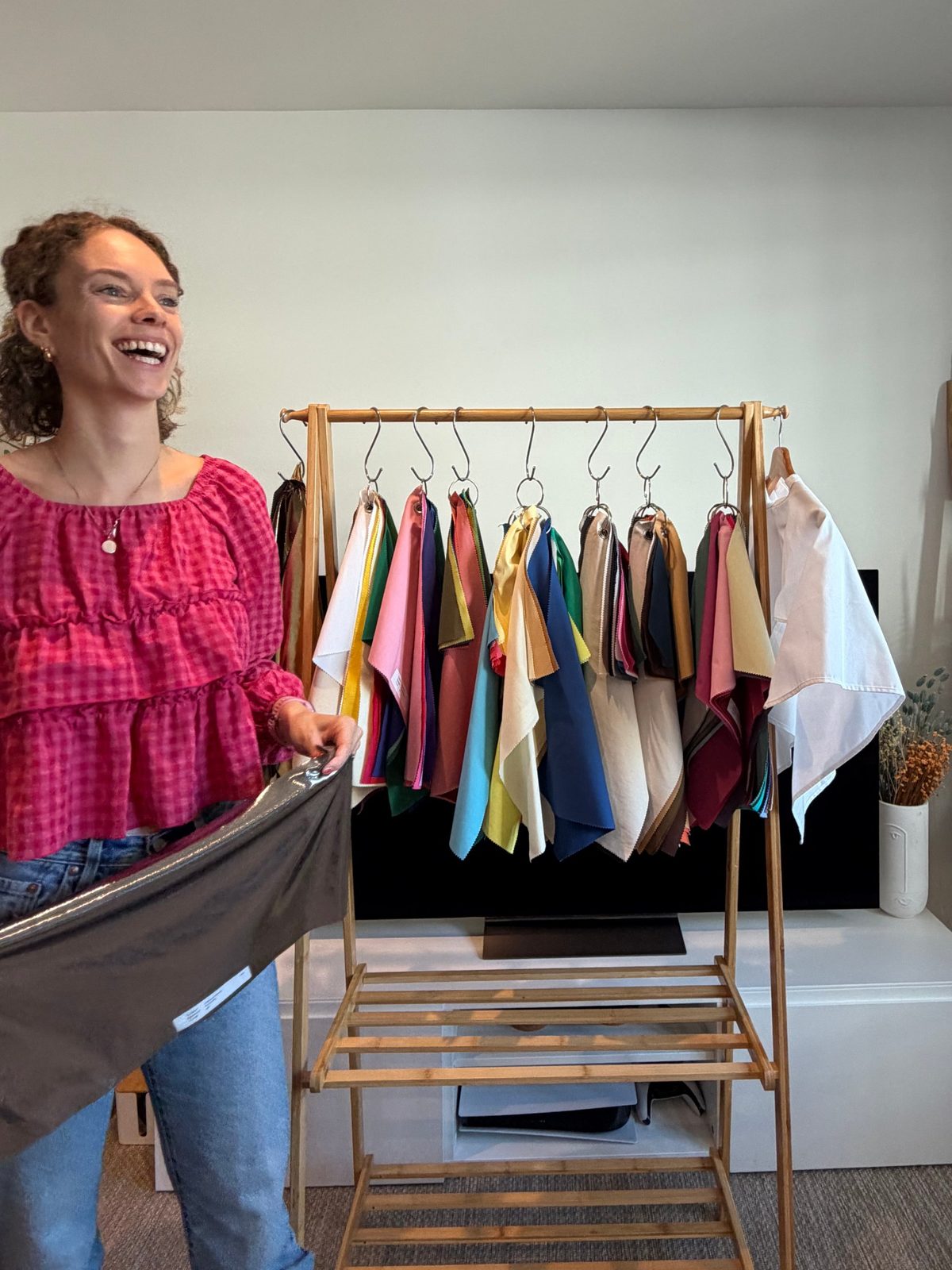 Shann laughing beside her rail of colour drapes, holding a metallic drape